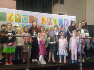 School group standing on stage in front of Mothers' Day banner